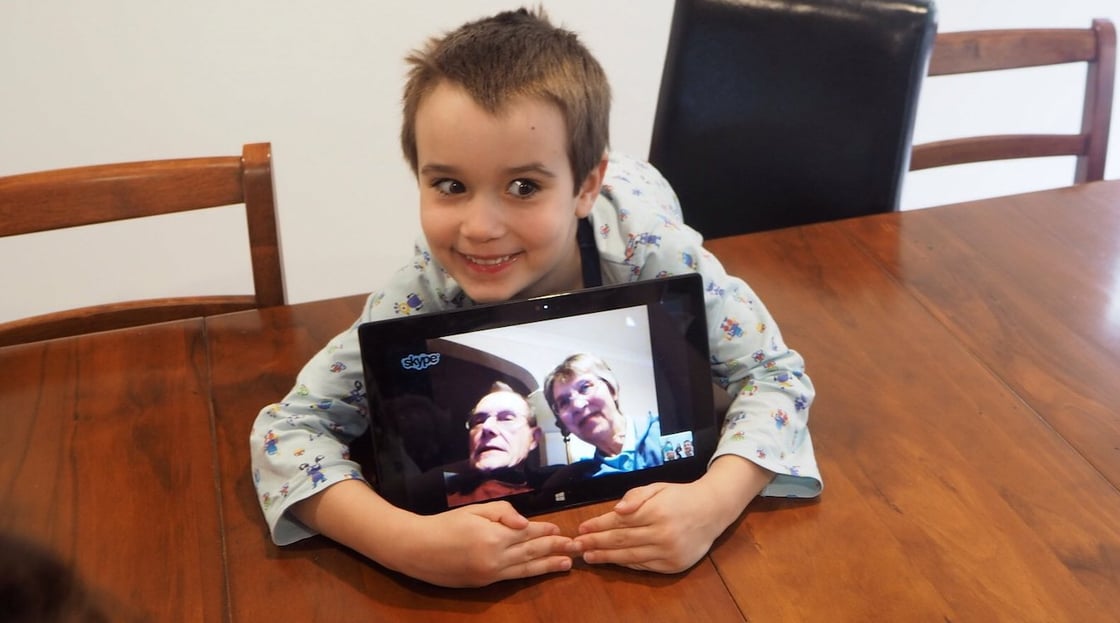 A child hugs a tablet computer during a video call with his grandparents